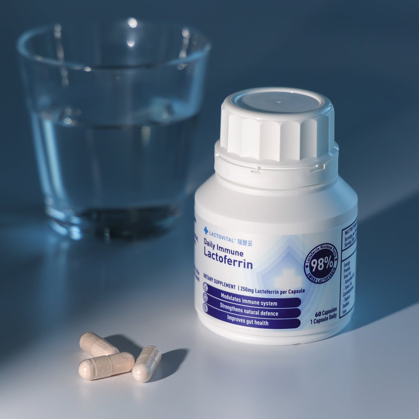 Bottle of Lactovital Lactoferrin Daily Immune capsules and a glass on a reflective surface
