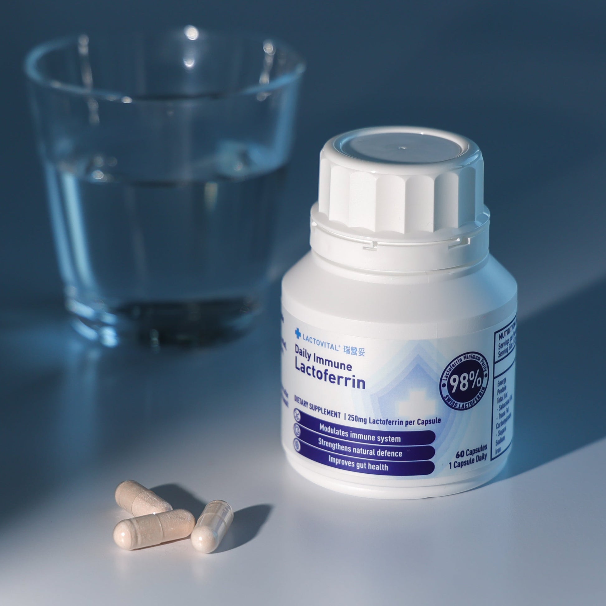 Bottle of Lactovital Lactoferrin Daily Immune capsules and a glass on a reflective surface