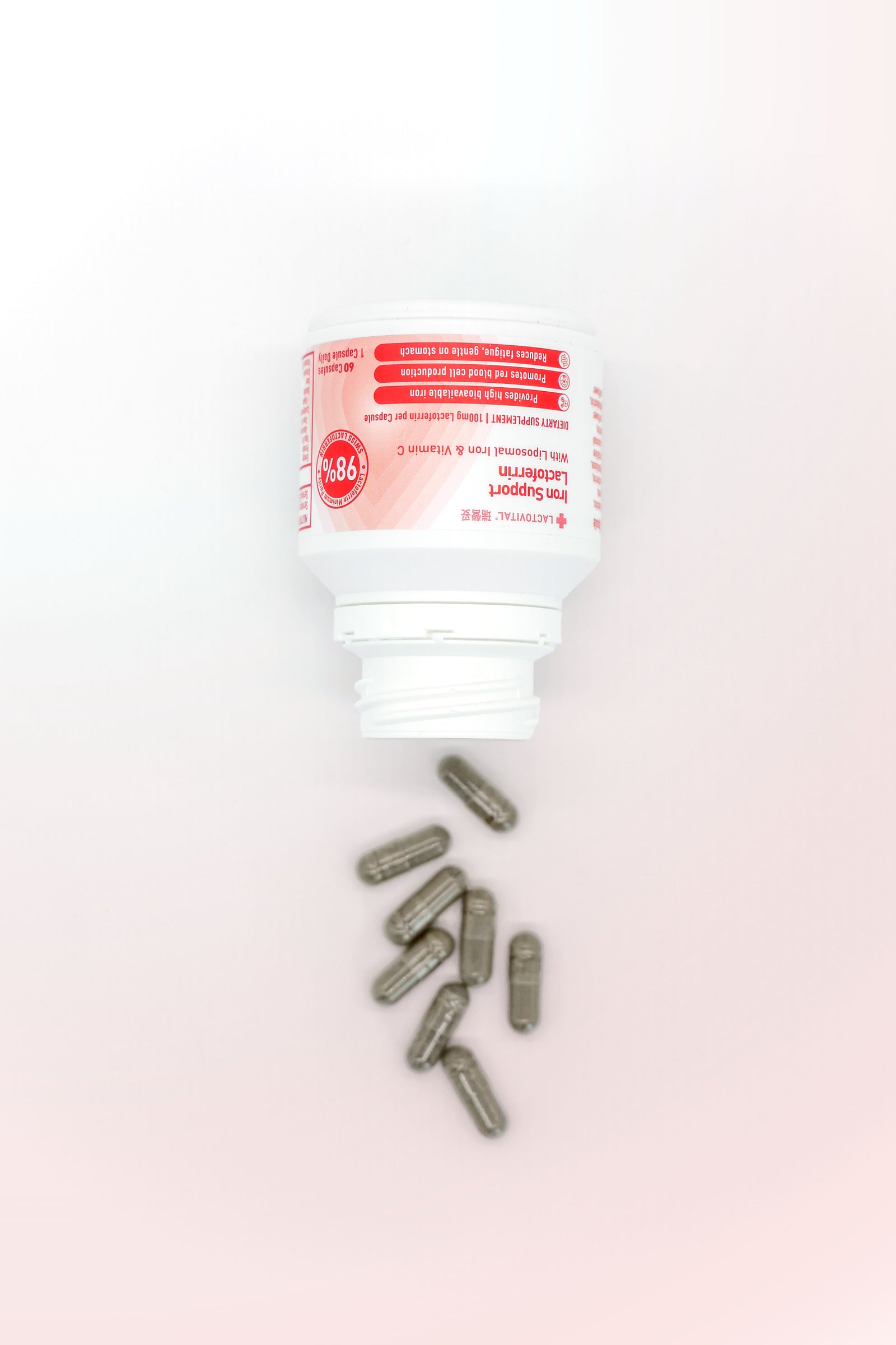 Bottle of Lactovital Lactoferrin Iron support supplements with a few capsules spilling out on a light pink background